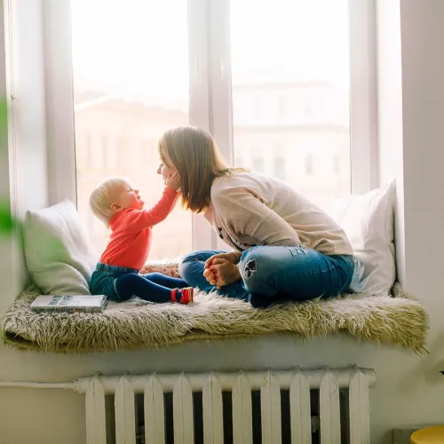 Baby reaches to touch its mother as they sit together at the window