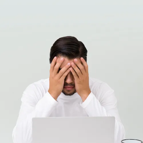 Man sits with his head in his hands in front of his laptop