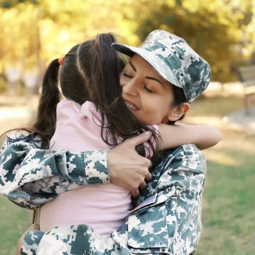 Woman in a military uniform happily embraces a young girl.