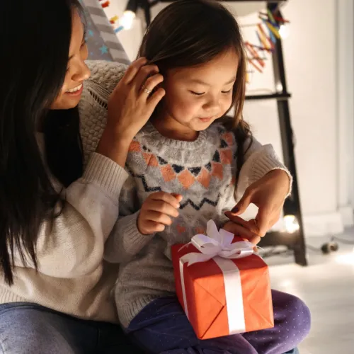 A young girl sits in her mothers lap as she receives a holiday gift.