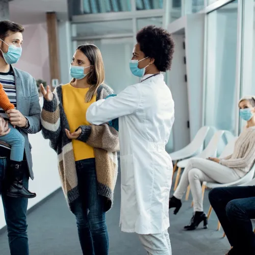 Two parents and a young child talk with a doctor, all wearing masks.