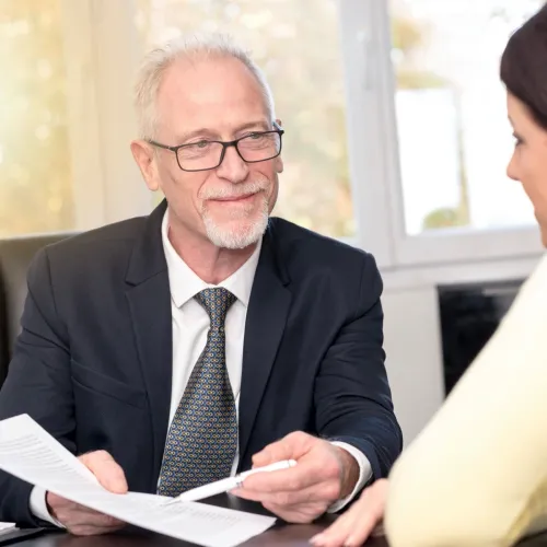 A older man simples and holds out a paper and pen towards a young woman.