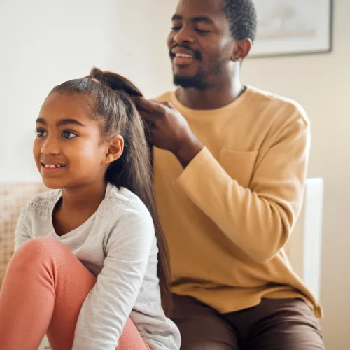 A father braids the hair of his young daughter.