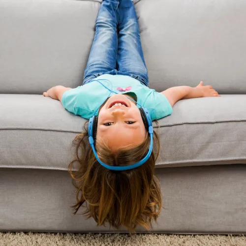 Girl laying upside on couch wearing headphones.