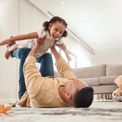 A father lays on the ground as he holds his happy, young daughter in the air