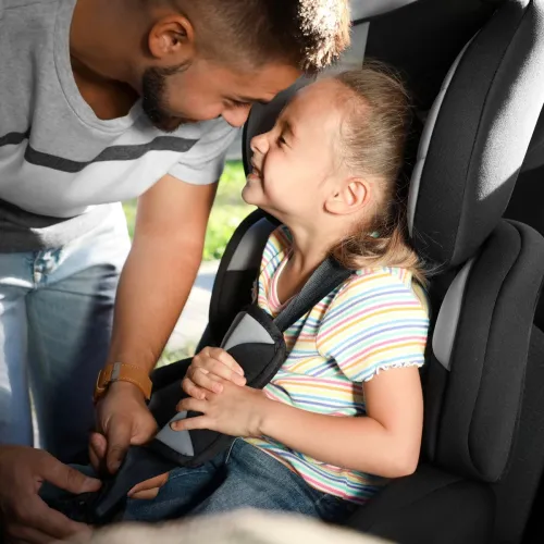 Man buckling his daughter into carseat. 