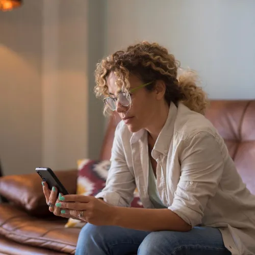 Woman on couch, looking at her phone seriously.