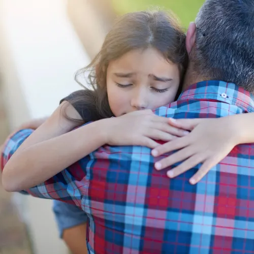 Young girl hugging her dad while looking upset.