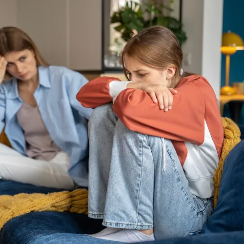 Teen girl upset with mom on couch.