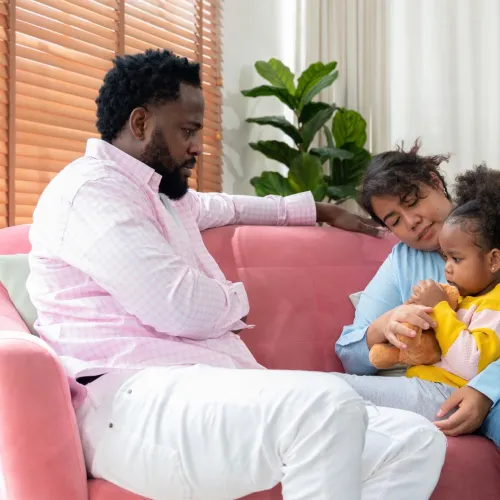 Dad and mom talking to young daughter on couch. 