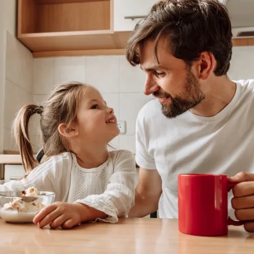 Man and young girl sitting at the kitchen table smiling.
