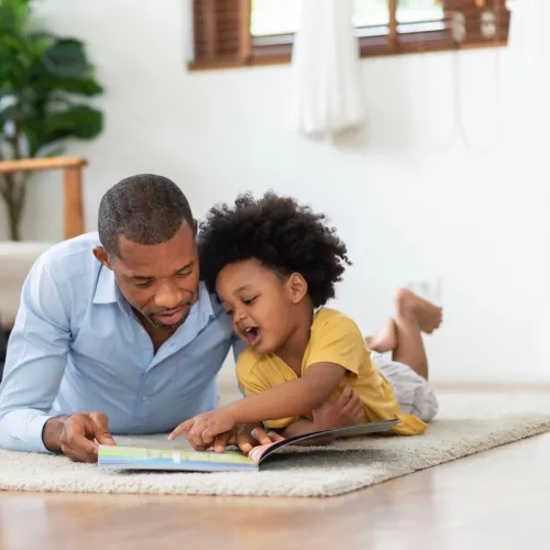 Dad and young child reading a book on floor. 
