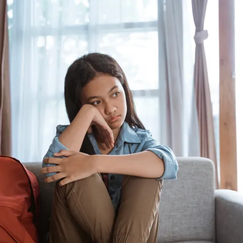 Young girl waiting on couch with her backpack.