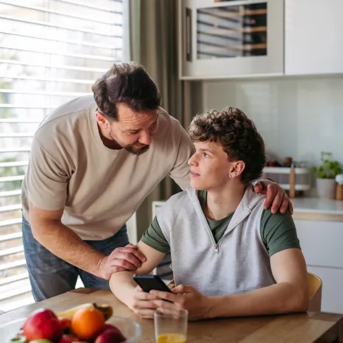 Man talking to teenage boy in kitchen.