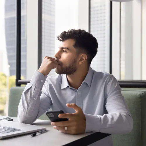 Man holding his phone and thinking, with a pensive look on his face. 