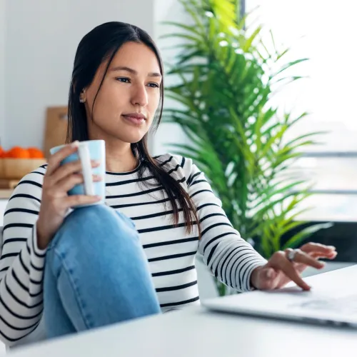 Woman drinking tea while considering response to message.