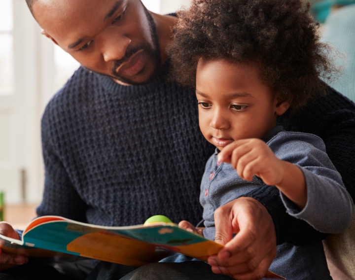 A father reads a book to his infant son.