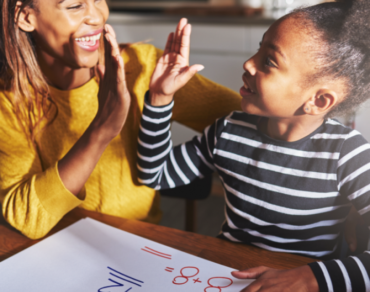 Mother high fives her young daughter while they work on math problems together.