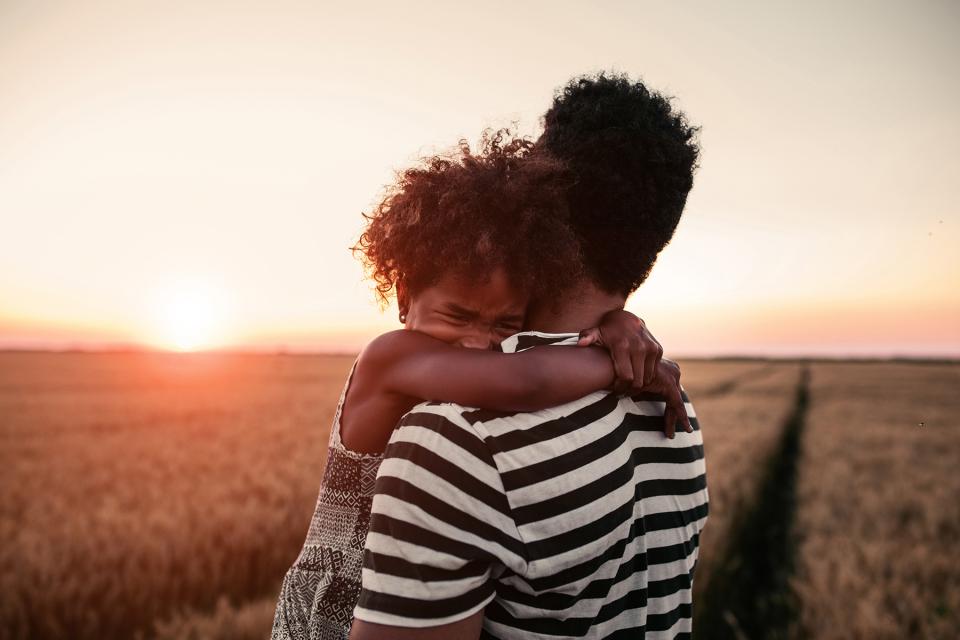 Young daughter holds father tight as he carries her through a field