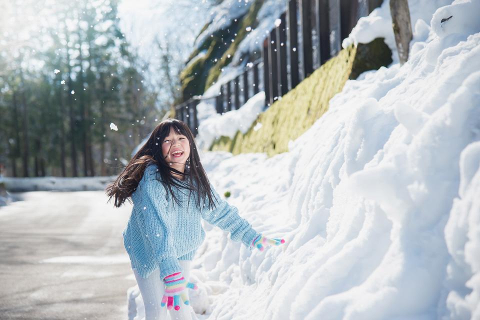 Young girl runs down snow-lined street with a smile on her face.