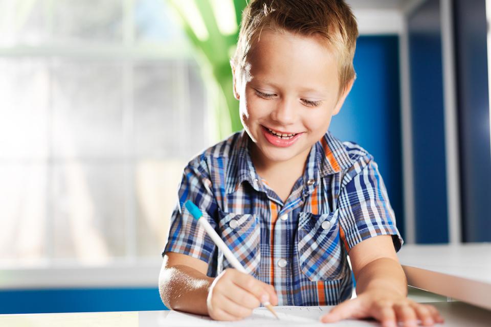 Smiling child sits at desk writing on a piece of paper.