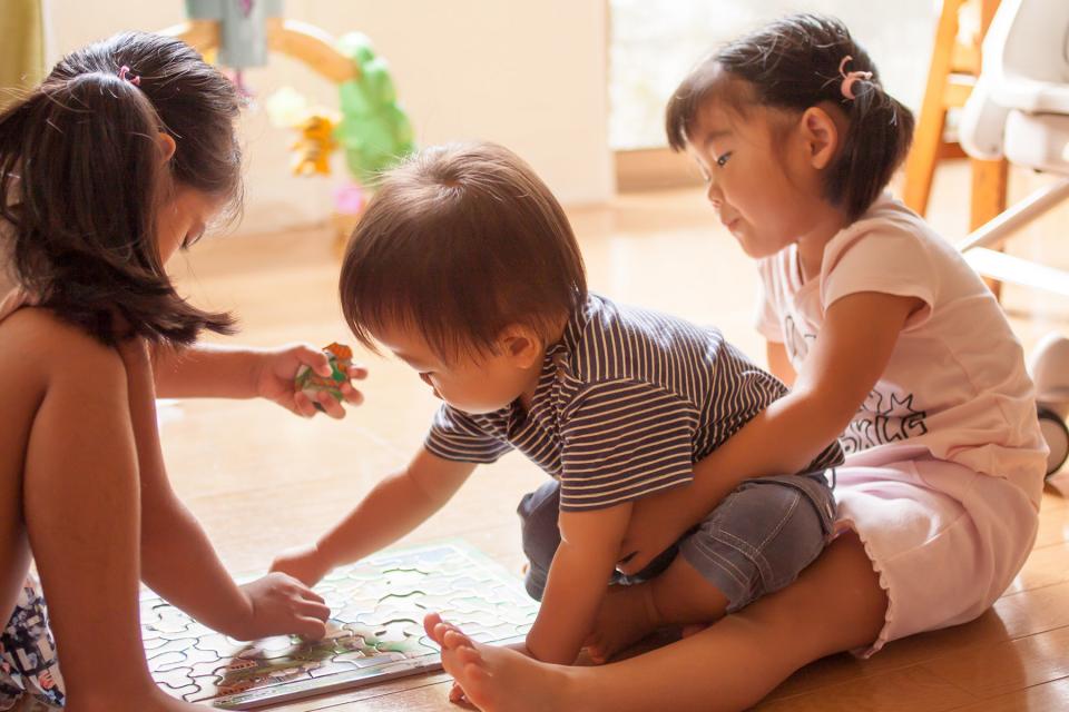 Siblings sit on the floor of their playroom while working on a puzzle together.