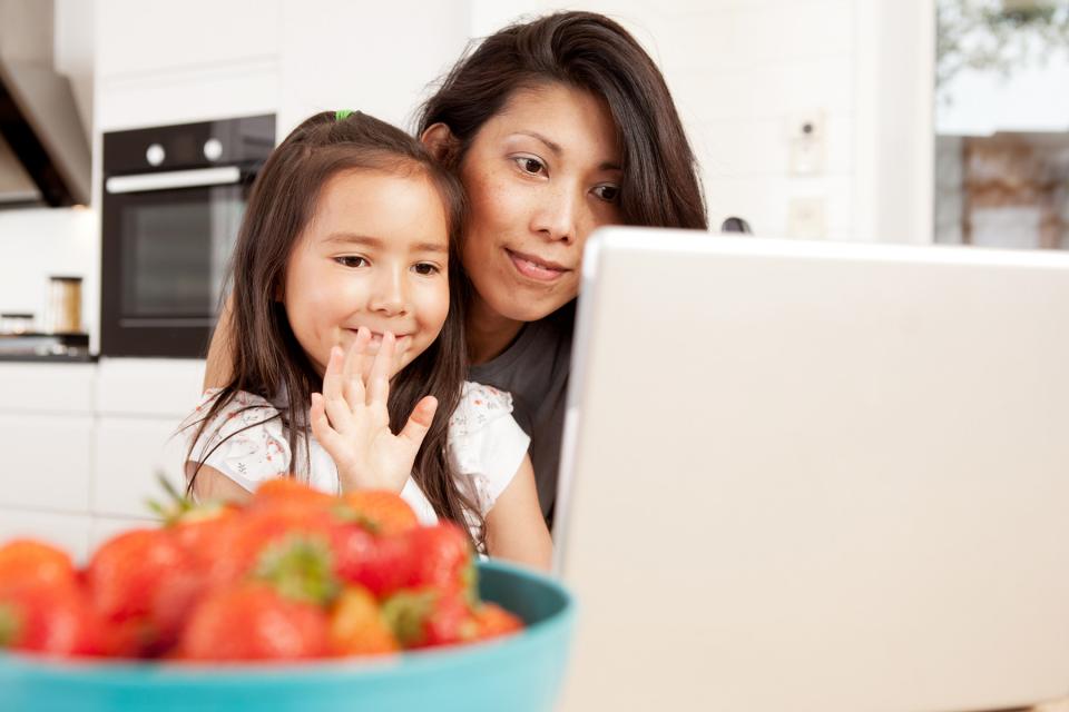 Child waving at parent on video chat while being held by mother