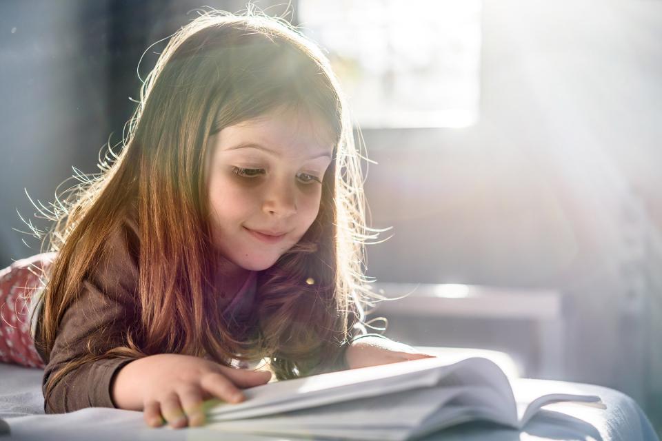 Young girl flips through her favorite book while lying on her bed.
