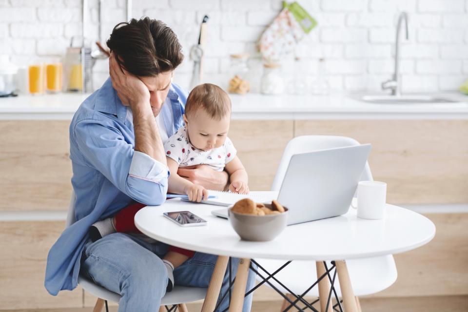 Man sits at his computer desk holding his baby with a disappointed look on his face.