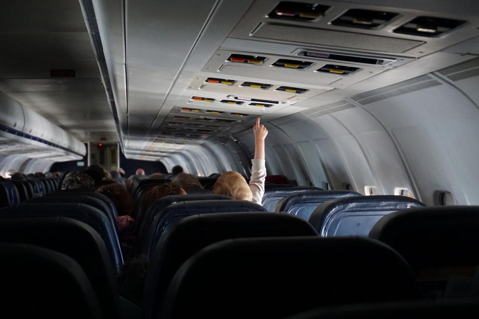Little boy reaches for the light above him while seated on an airplane.