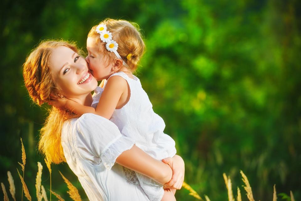 Young girl plants a kiss on her mother's cheek while being held