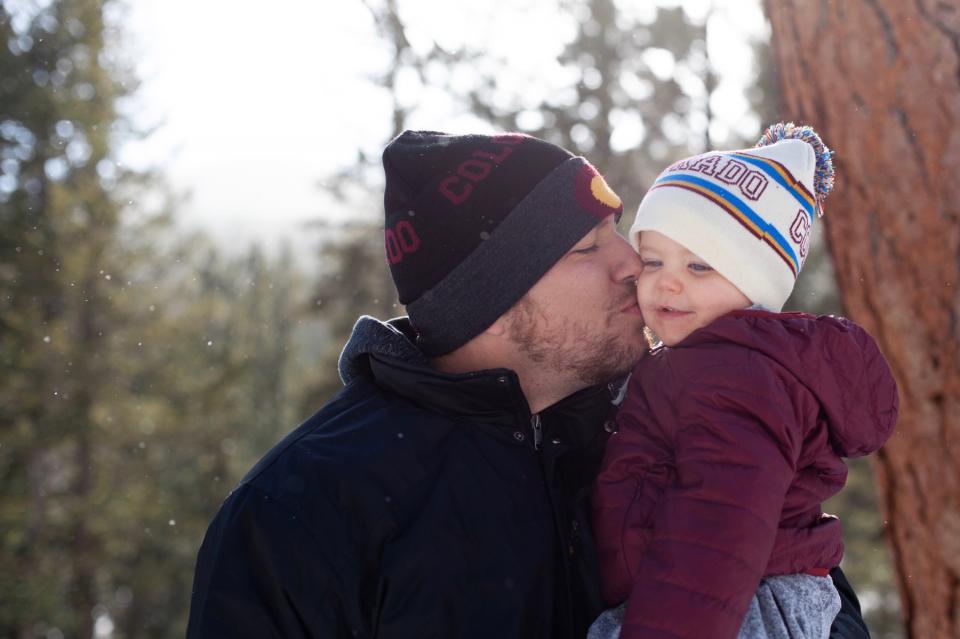 A father kisses his child in the woods on a chilly day.