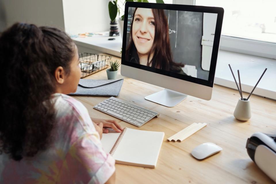 Young girl uses her home computer to have a videoconference with her teacher.