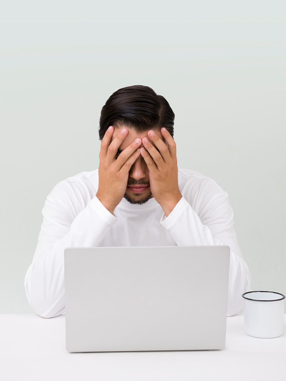 Man sits with his head in his hands in front of his laptop