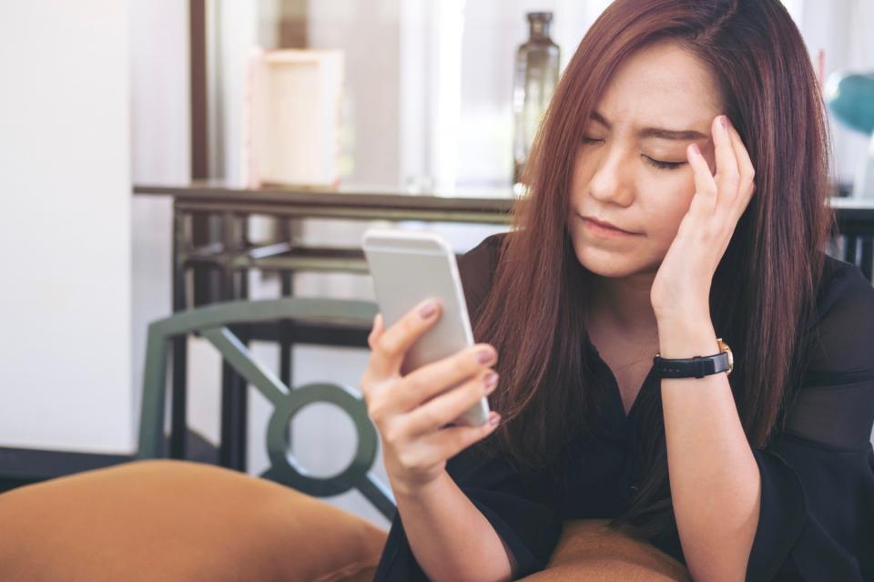A woman sits at a table and looks at her phone with a worried expression.