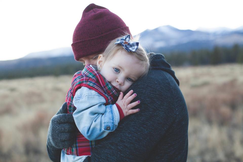 A dad hugs his baby outside in a field.