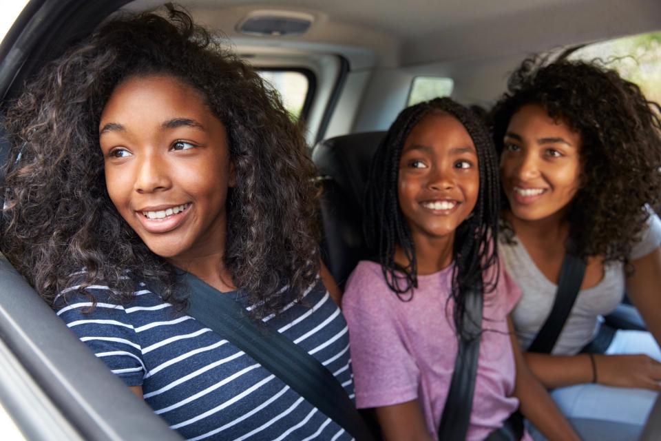 Two girls and their mom look at the car window.