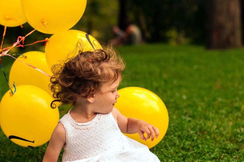 Young girl sits in the grass with a bunch of yellow balloons