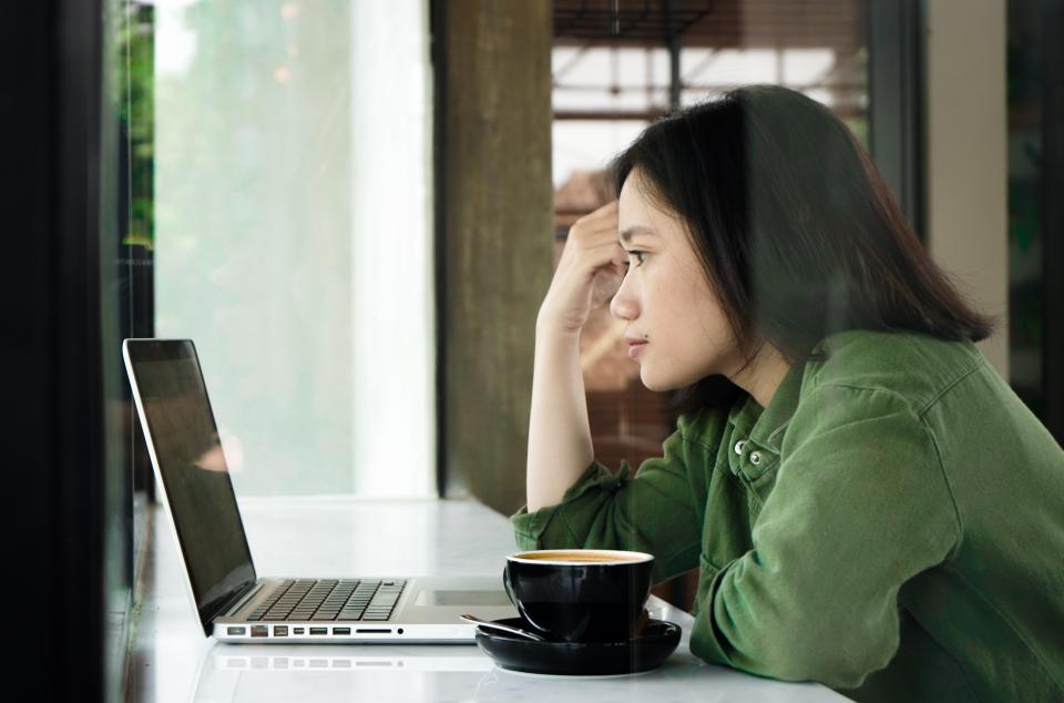 woman in green shirt looking at a laptop on a counter at coffee shop