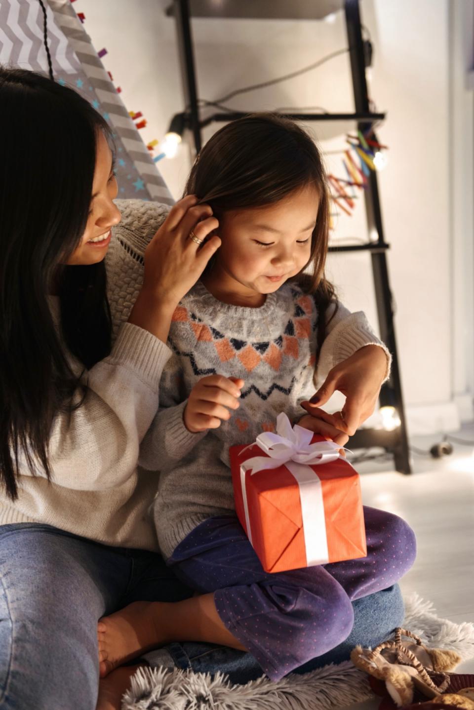 A young girl sits in her mothers lap as she receives a holiday gift.