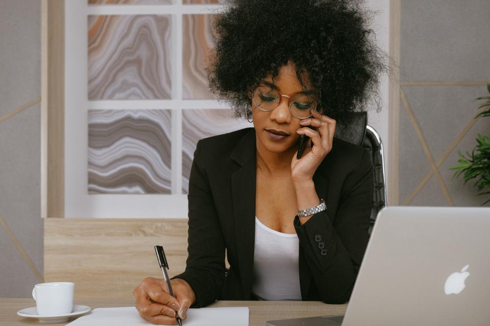 woman on phone in front of laptop with coffee