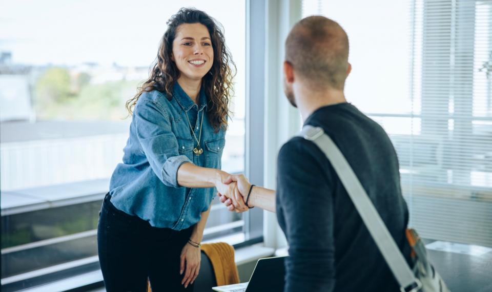 A man shakes hands with a woman in a blue denim shirt. She smiles a the man.