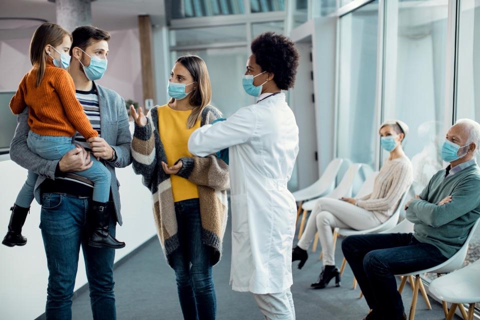 Two parents and a young child talk with a doctor, all wearing masks.