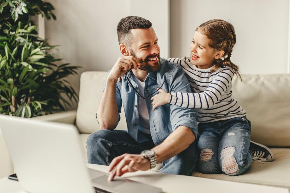 A young girl hugs her father from his side while sitting together on the couch. They look at each other and smile.