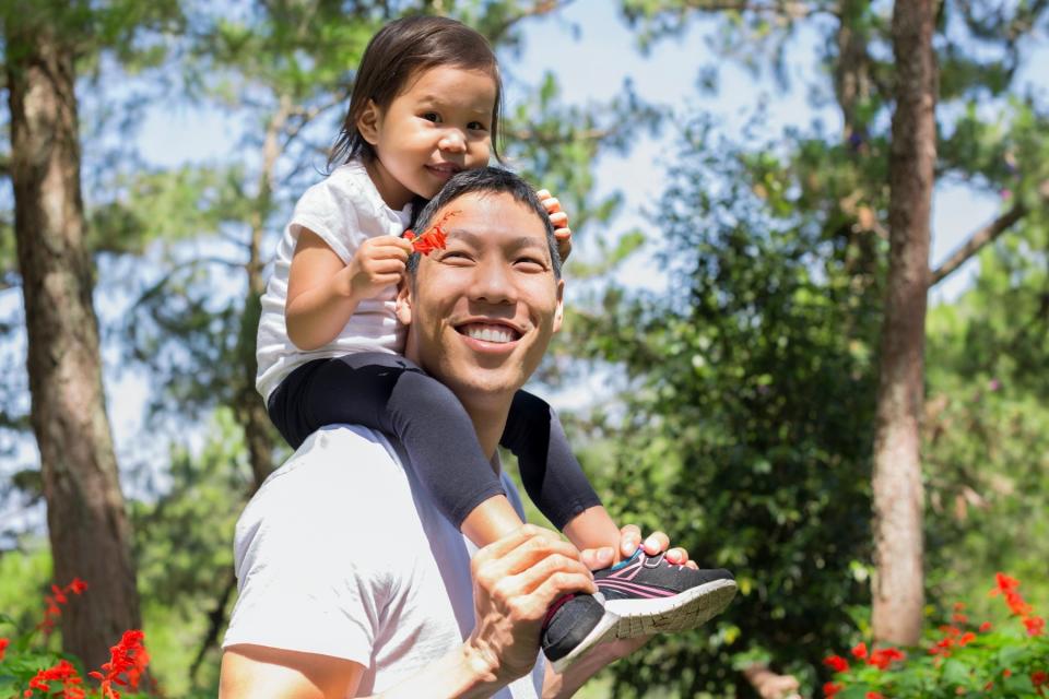 A man holds a young child on his shoulders while walking outside.