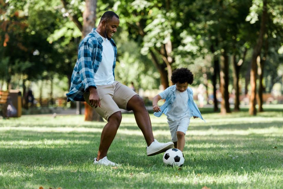 A father and his young son play with a soccer ball in the park.