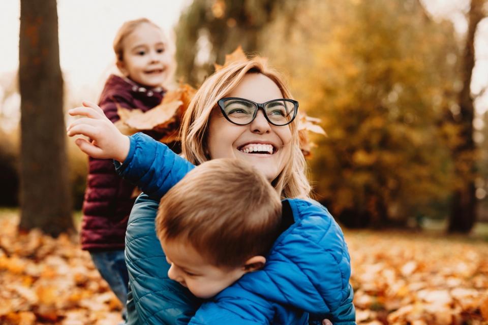 A mother and two children playing happily in a pile of autumn leaves.