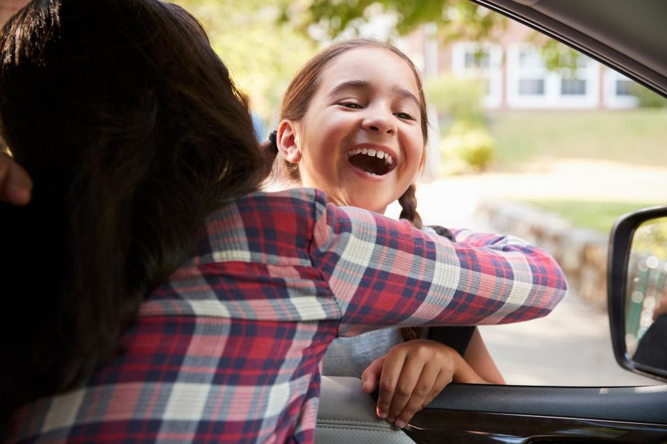 Girl hugs her mother through the open window of a car.