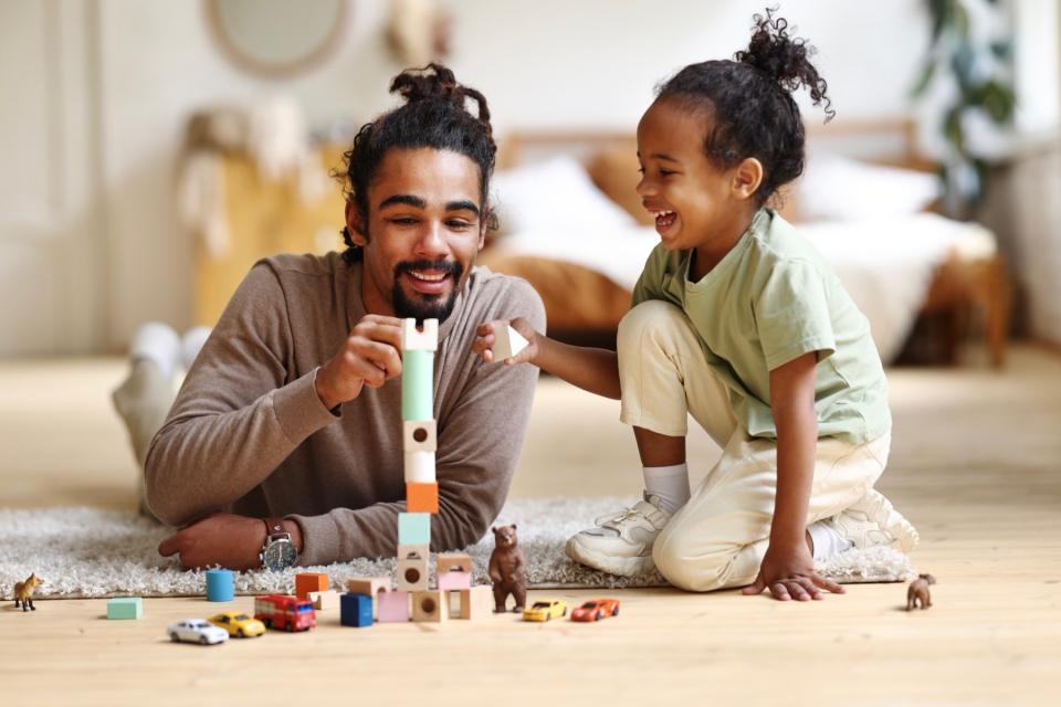 A father plays with blocks on the floor with his young daughter.
