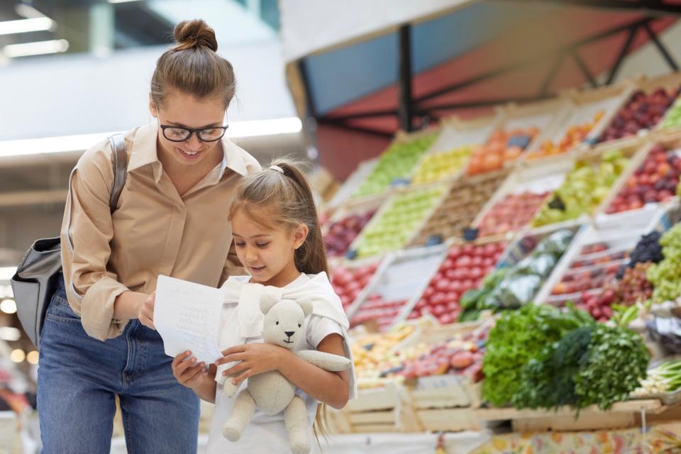 A mother and her young daughter review a grocery list while in the store.